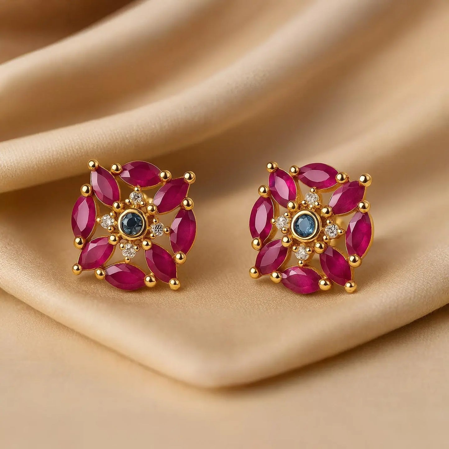 Pair of gold earrings with red gemstones on a beige fabric background