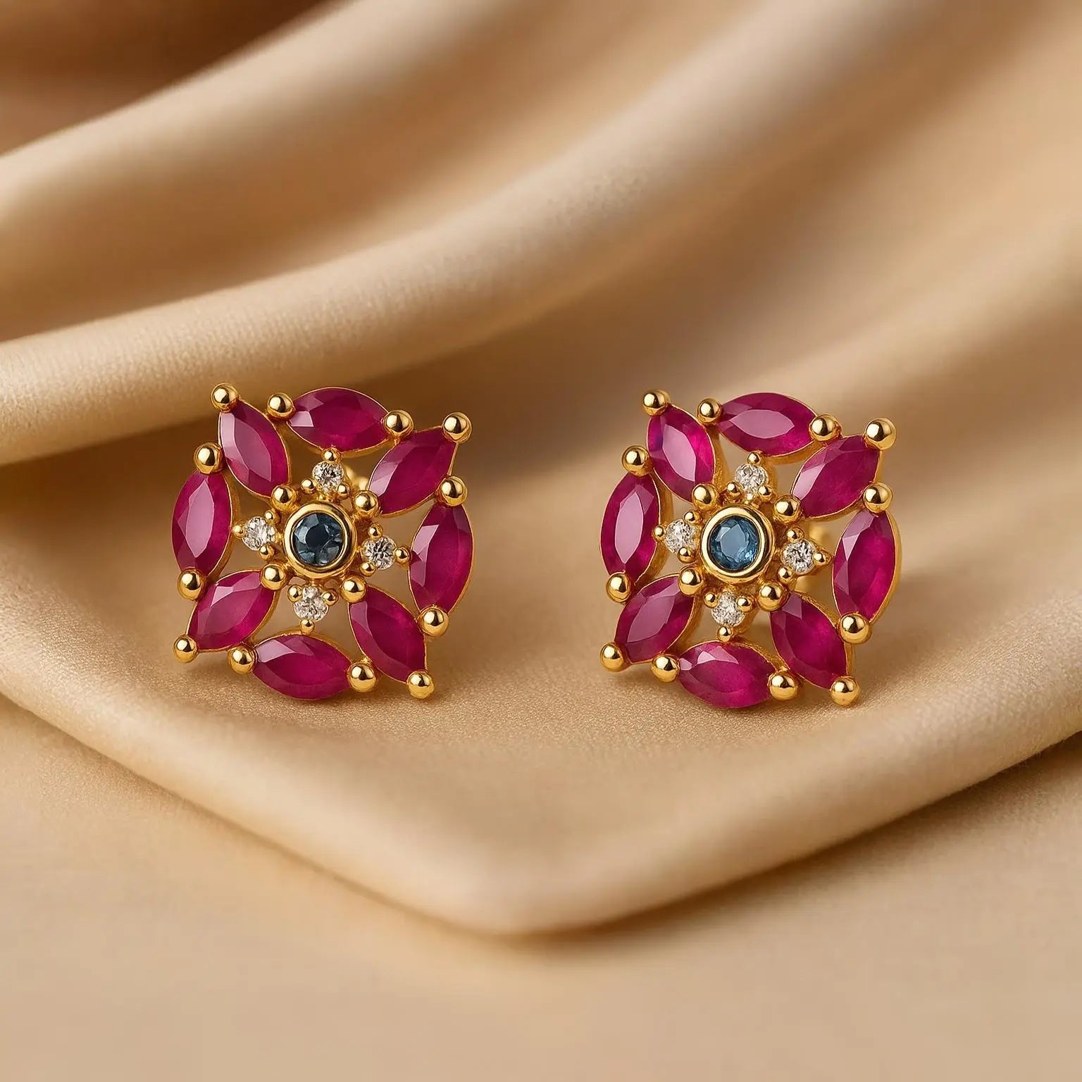 Pair of gold earrings with red gemstones on a beige fabric background