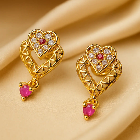 Gold heart-shaped earrings with red gemstones on a beige background