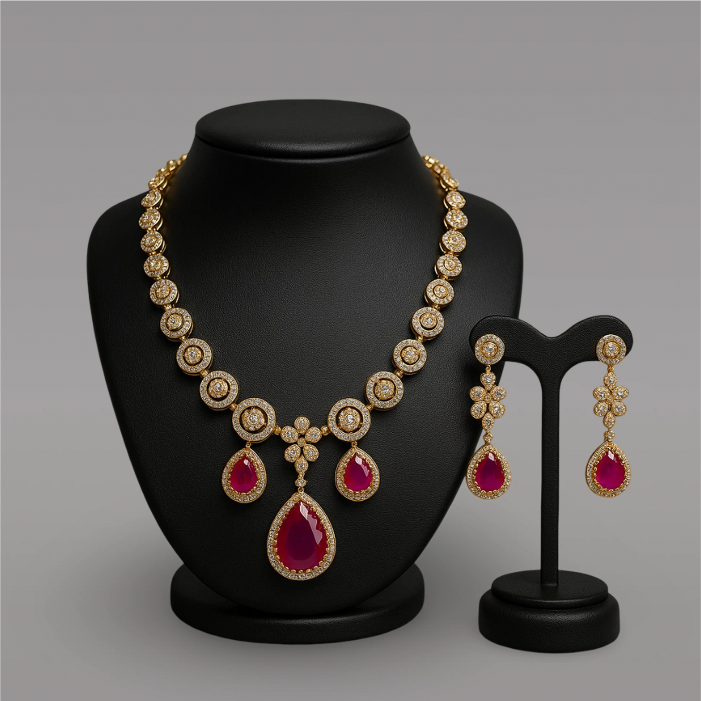 Gold necklace with red gemstones and matching earrings on a black stand against a gray background