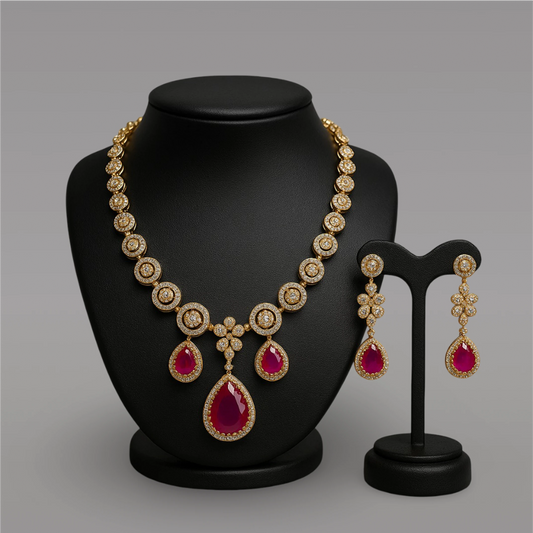 Gold necklace with red gemstones and matching earrings on a black stand against a gray background
